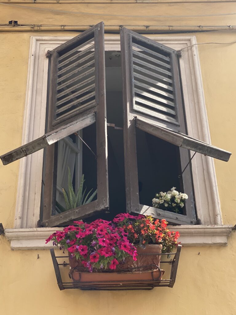 Italiaans raam met houten luiken en roze bloemen in Corinaldo