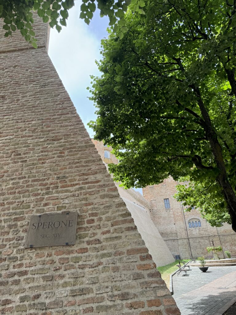 Rustig pleintje met bomen en oude bakstenen muren in Corinaldo